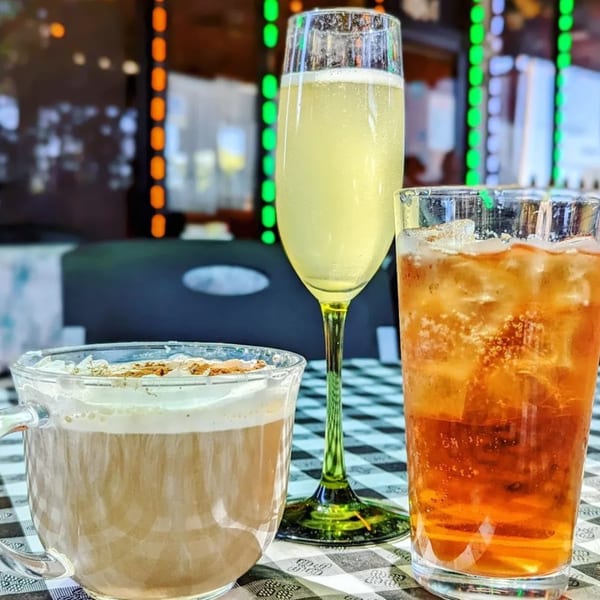 Three drinks on a checkered tablecloth: a latte, a mimosa, and an iced tea at Crepe Town.