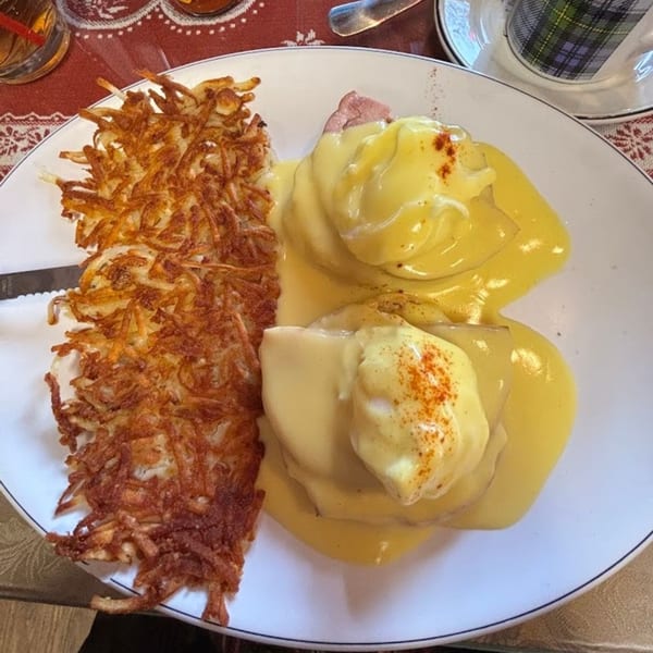 Eggs Benedict with hollandaise sauce and a side of crispy hash browns on a white plate.