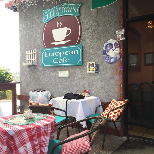 Outdoor seating area of Crepe Town European Café with checkered tablecloths and decorative pillows.