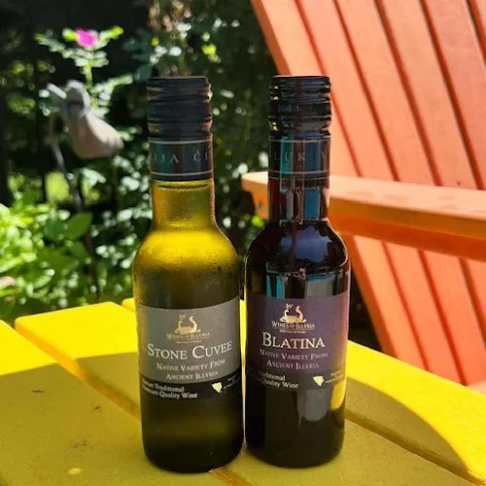 Two bottles of Georgian wine labeled Stone Cuvee and Blatina on a yellow outdoor table beside an orange chair.