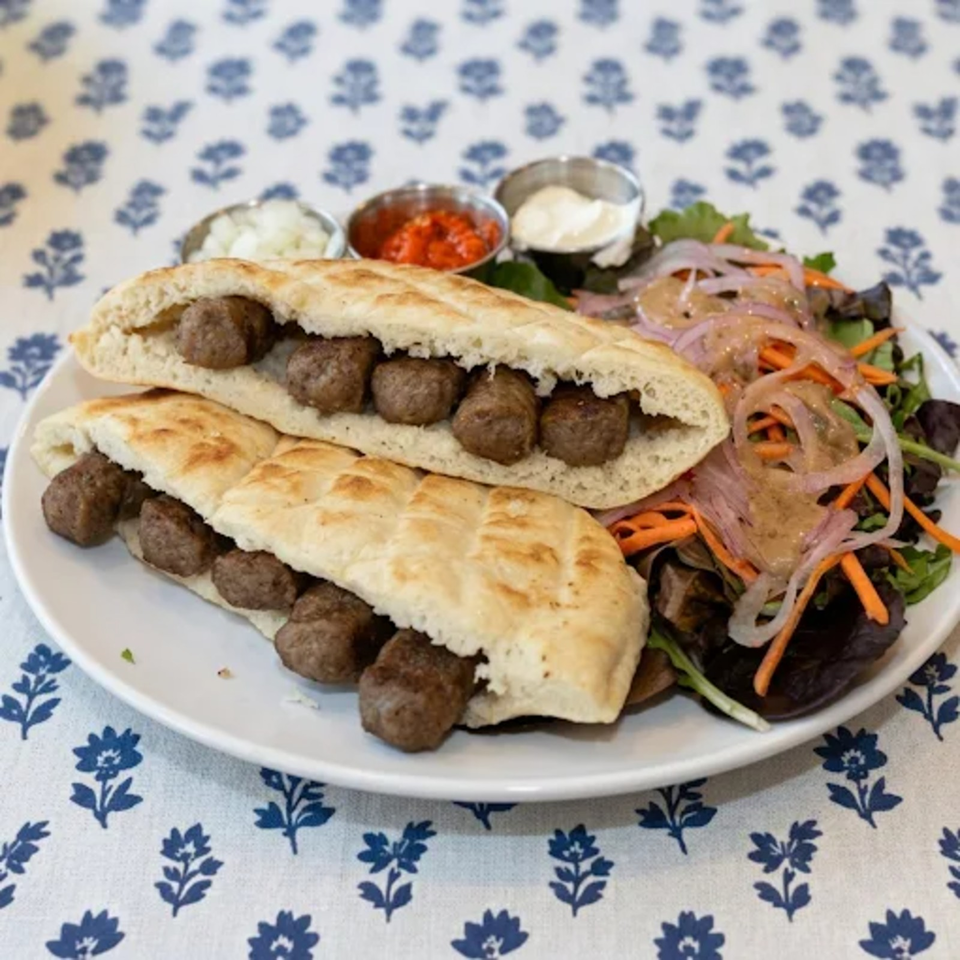 Two meatball-filled flatbreads with mixed salad, sliced onions, carrots, and dipping sauces on a plate.
