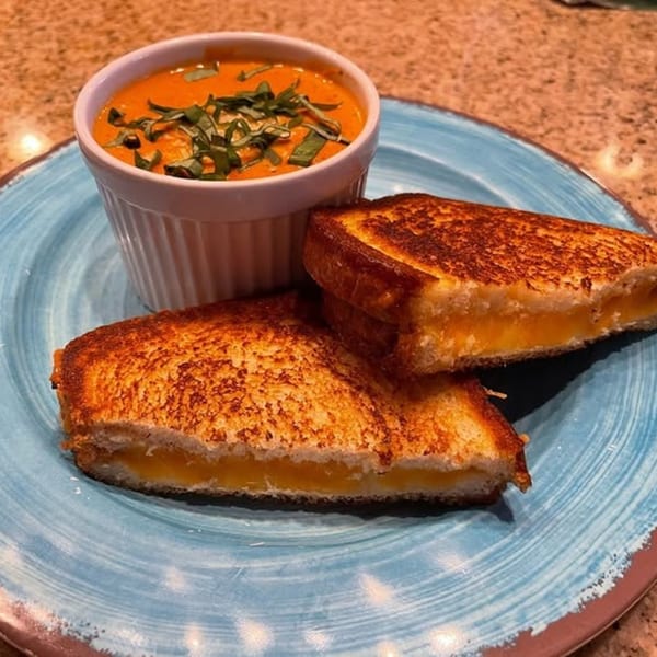 Grilled cheese sandwich halves with melted cheese and a side of tomato soup topped with basil.