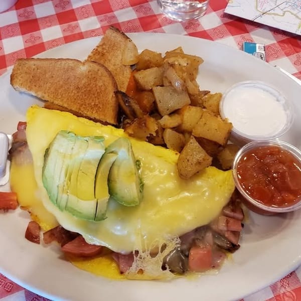 A European breakfast plate with an avocado omelet, home fries, toast, salsa, and sour cream.