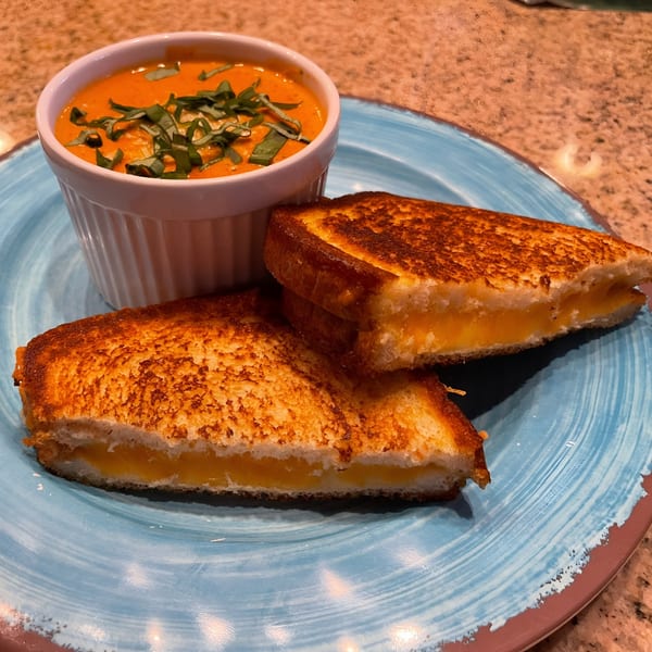 Grilled cheese sandwich halves with melted cheese and a side of tomato soup topped with basil.