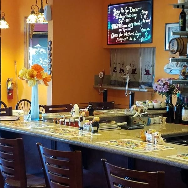 A cozy European cafe interior with a bar counter, stools, and a specials board on an orange wall.