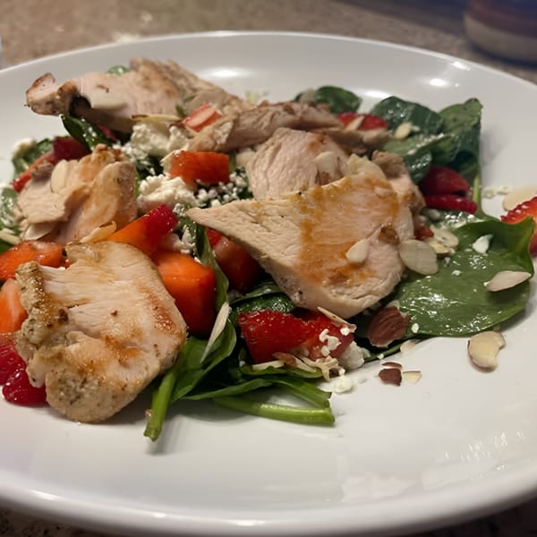 Grilled chicken and strawberry salad with spinach, feta, and almonds on a white plate.
