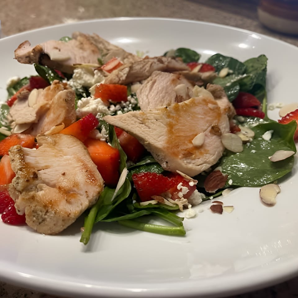 Grilled chicken and strawberry salad with spinach, feta, and almonds on a white plate.